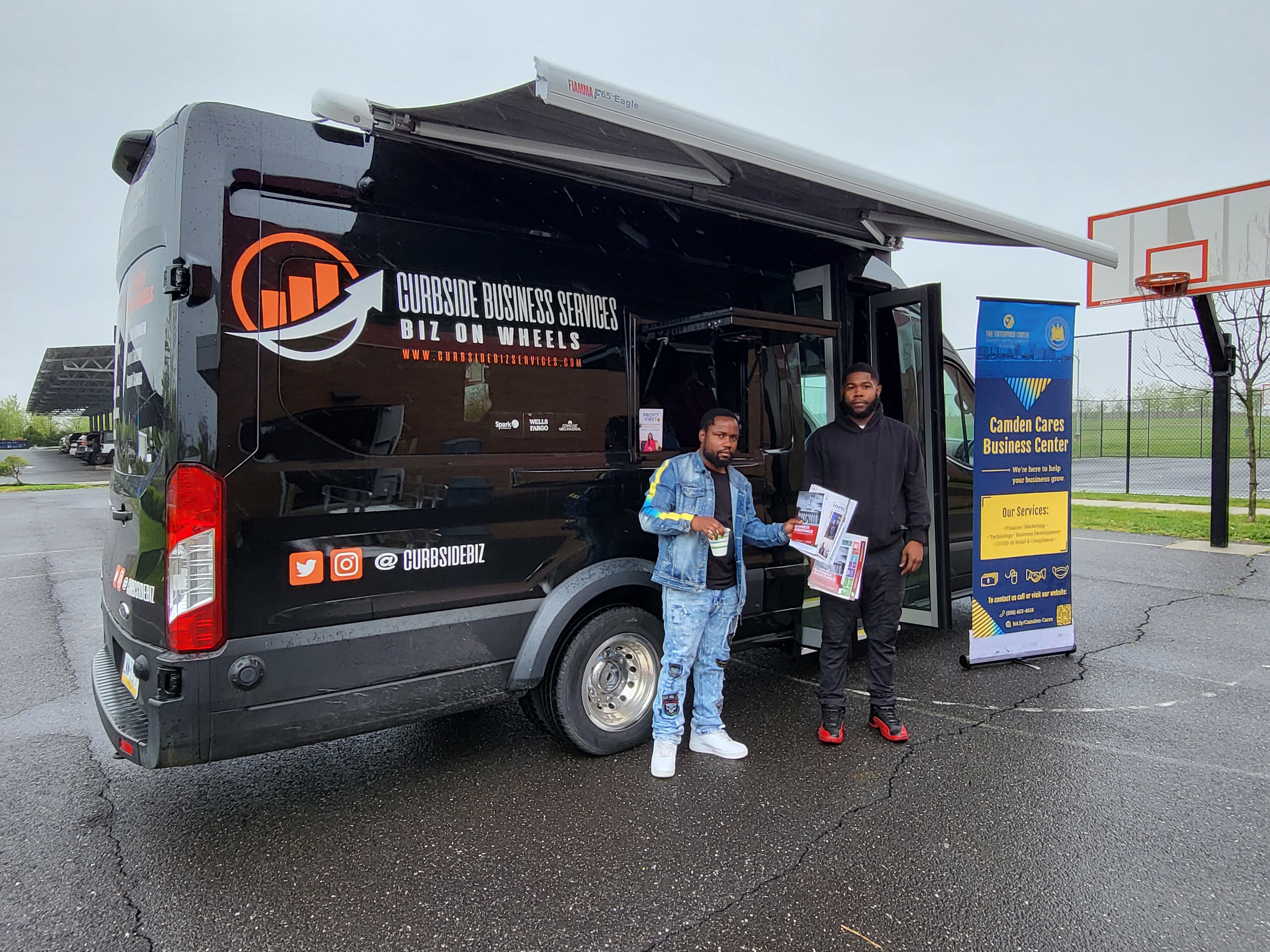 Two men standing next to biz on wheels